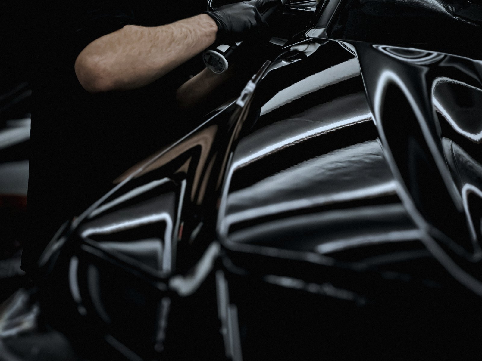 Gloved hand holding an inspection lamp, its reflection raking across dark glossy paint