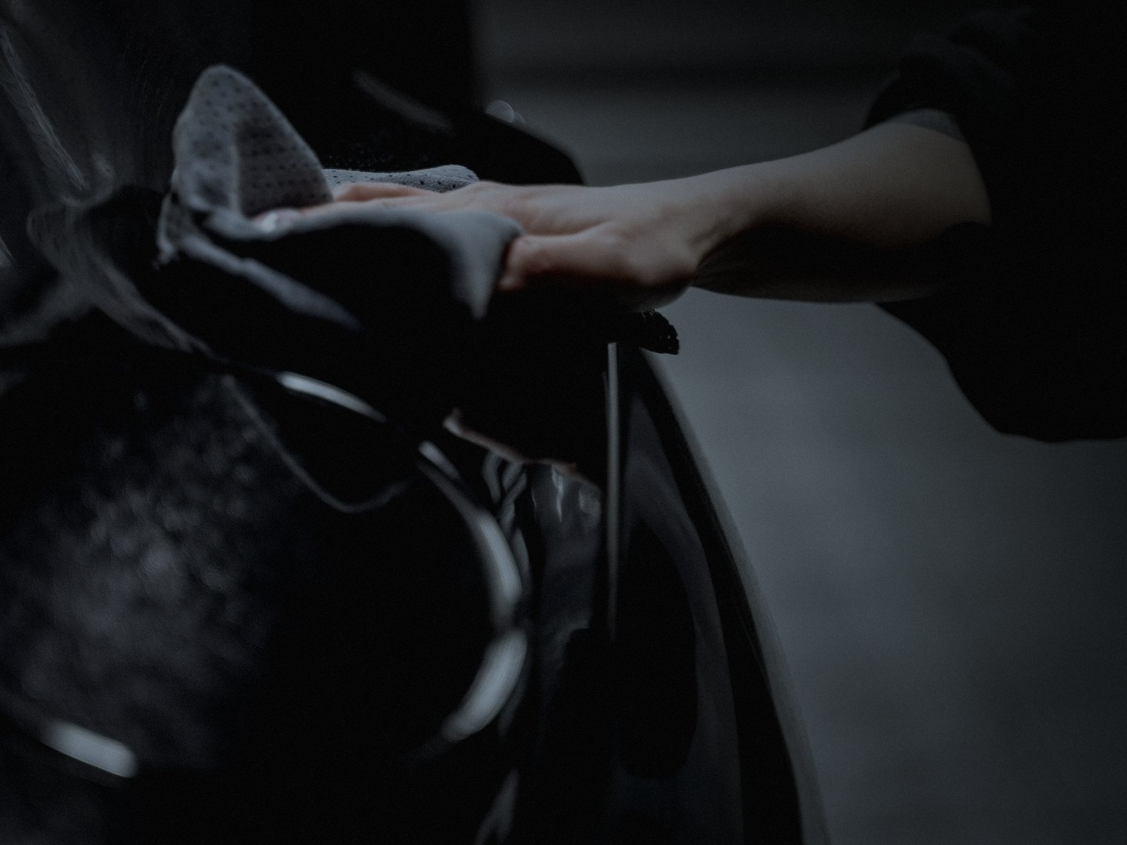 Gloved hand drying dark glossy paint with a microfiber towel